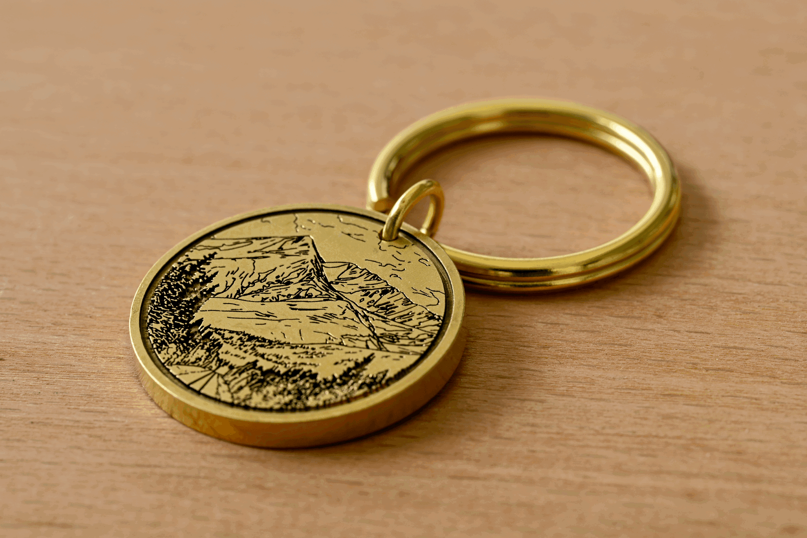 Brass circular keychain featuring an engraved mountain landscape on a wooden surface