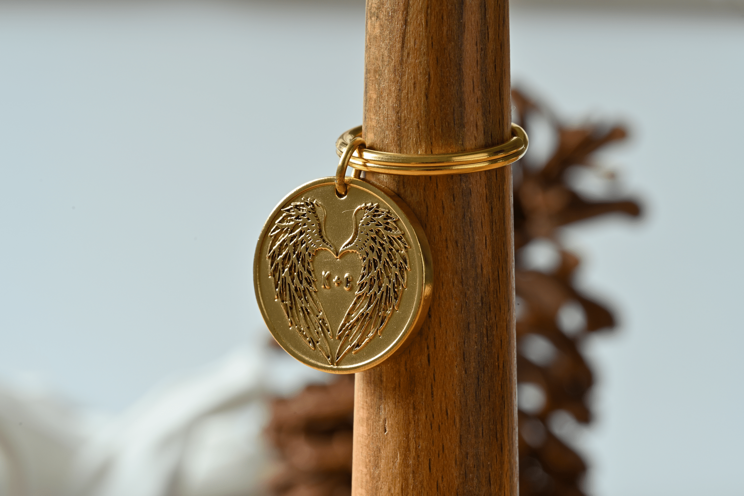 Gold circular keychain charm engraved with angel wings forming a heart shape around the initials K + C