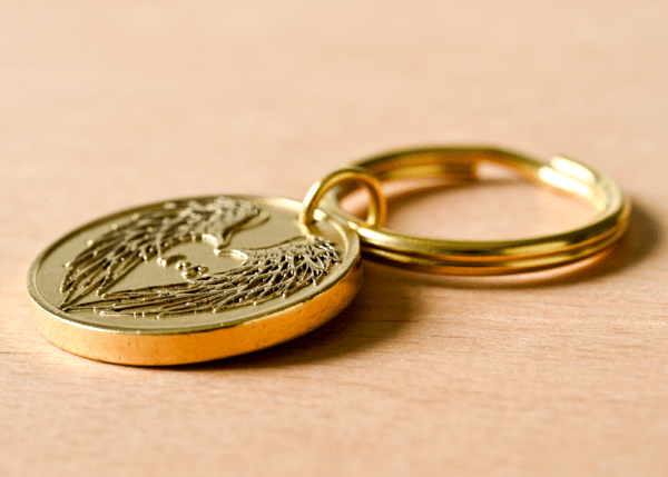 Gold keychain medallion with embossed angel wings forming a heart around a semicolon symbol