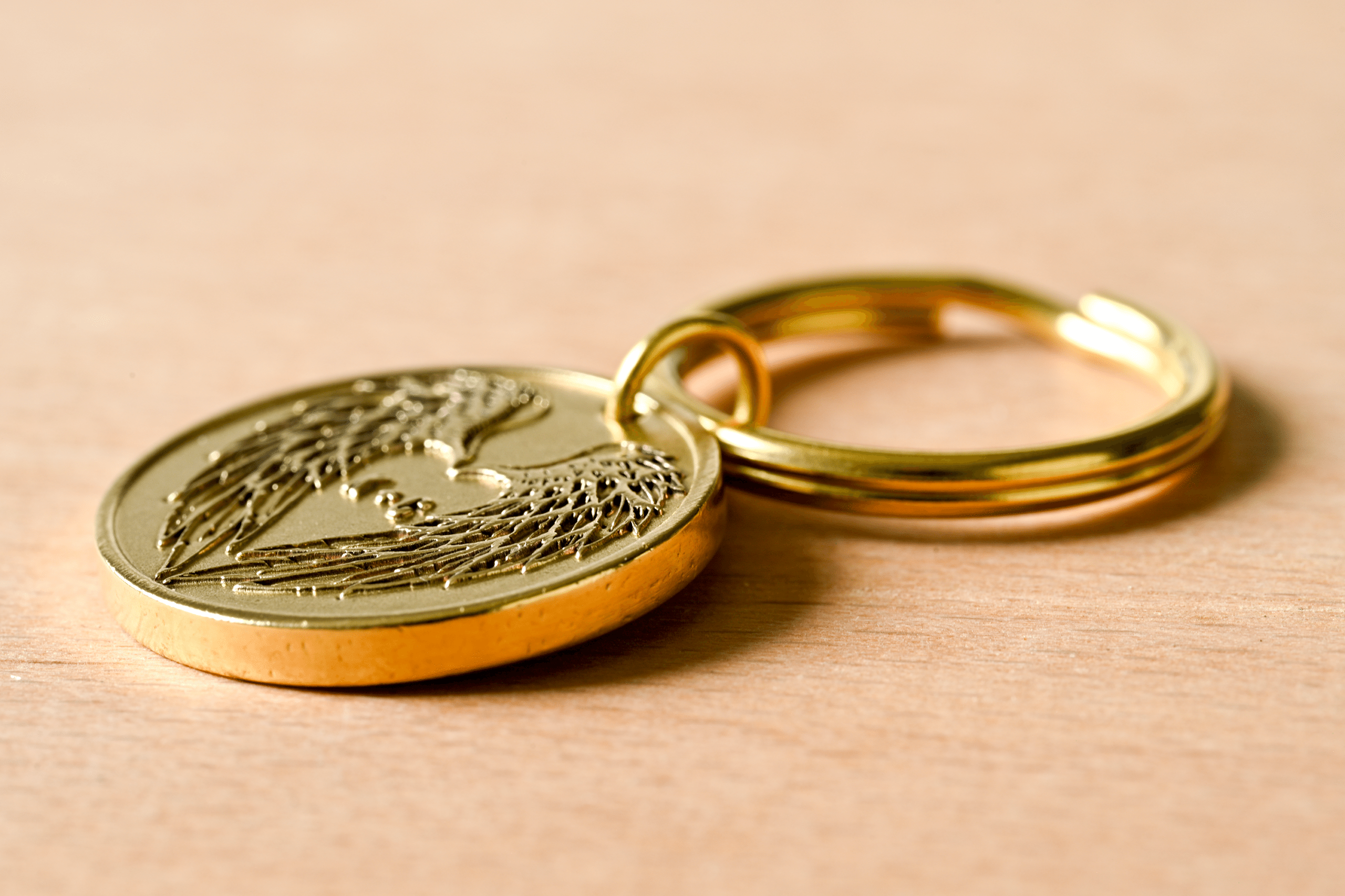 Gold keychain medallion with embossed angel wings forming a heart around a semicolon symbol