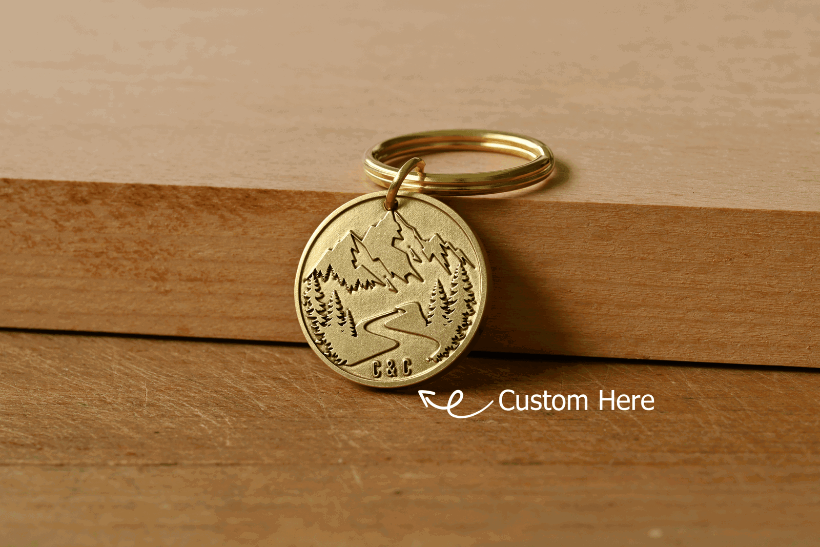 Brass keychain engraved with a mountain scene, with an arrow pointing to custom initials C&C engraved at the bottom