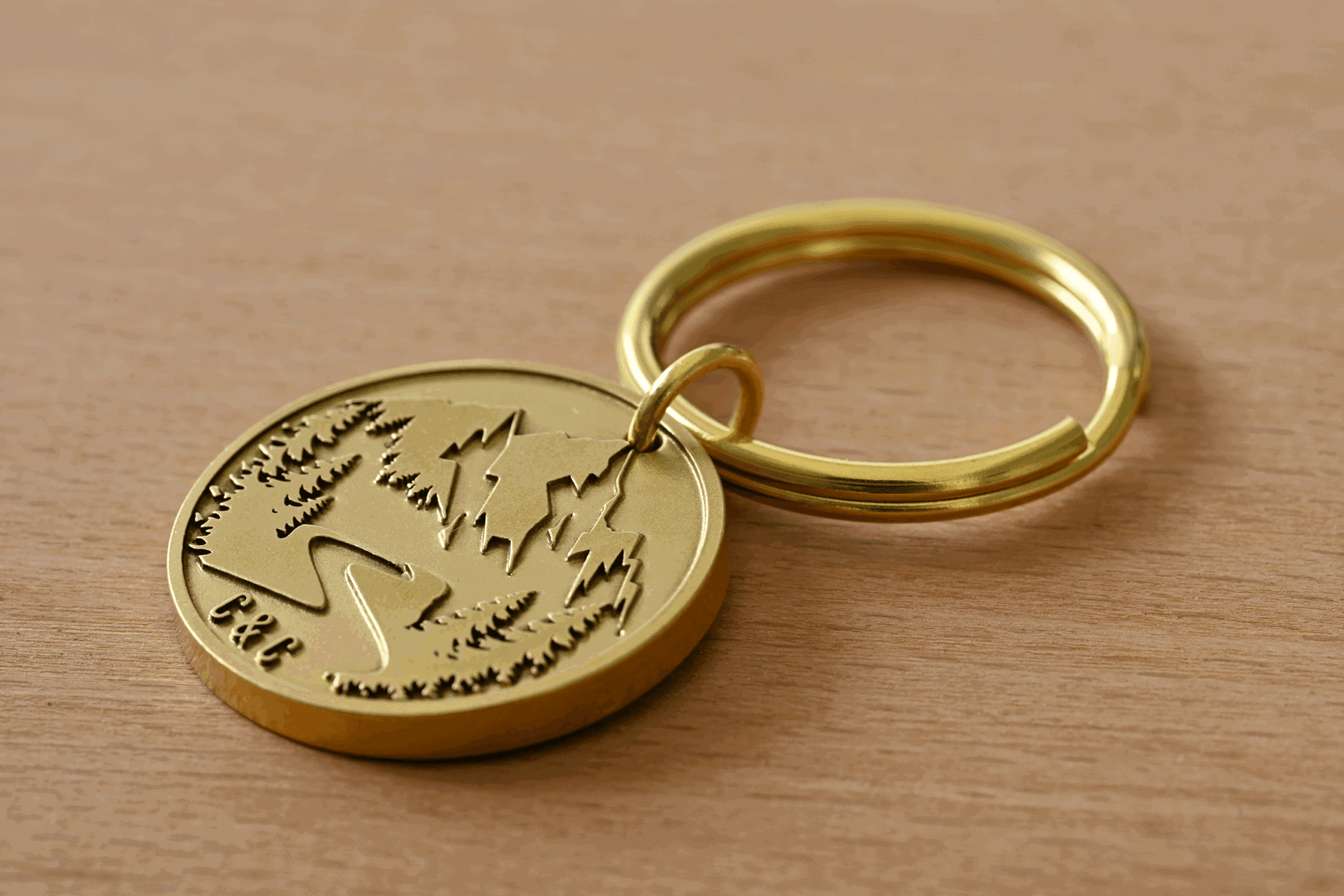 Brass circular keychain engraved with a mountain and forest scene and the initials C&C