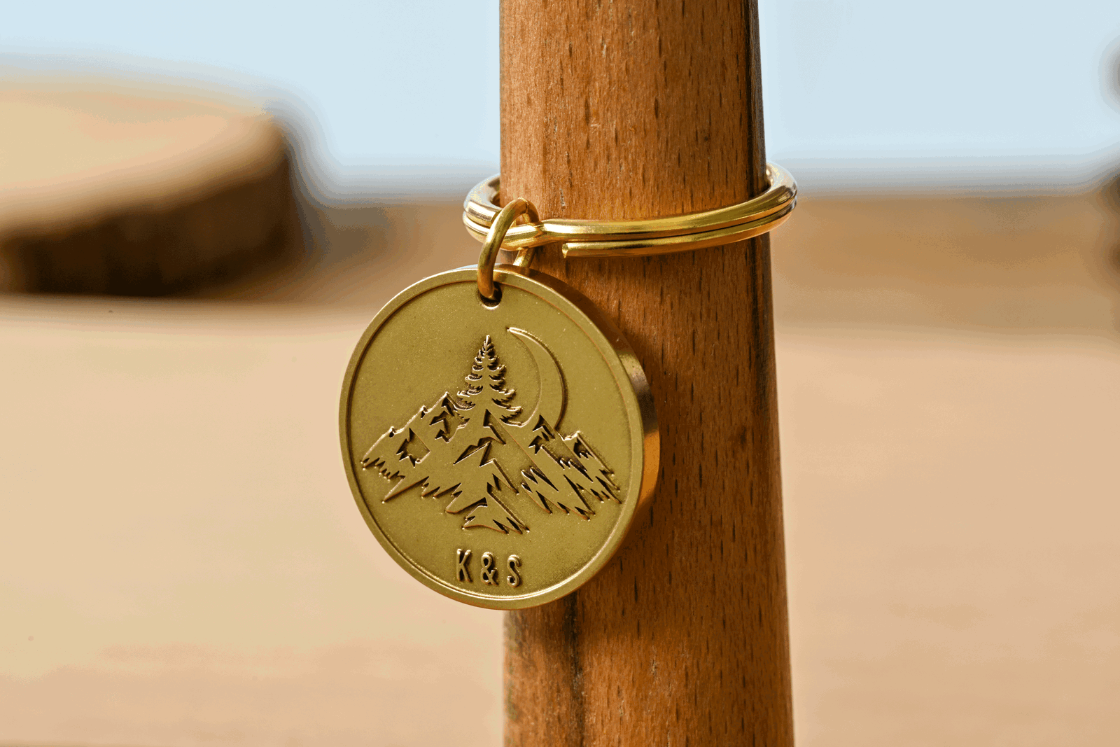 Round brass keychain tag engraved with a mountain landscape, crescent moon, and the initials K&S