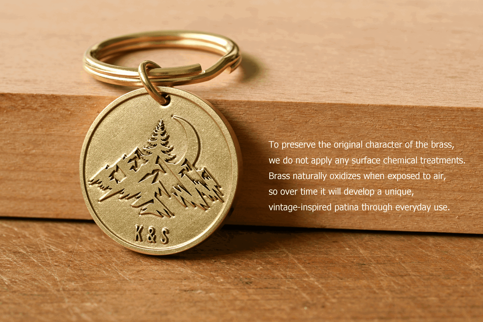 Round brass keychain engraved with a mountain scene and the initials K & S, next to text explaining that untreated brass naturally oxidizes over time to develop a unique vintage patina