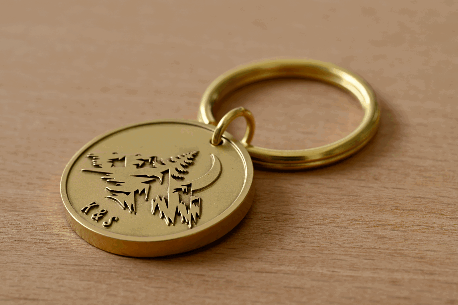 Brass keychain engraved with a mountain landscape, crescent moon, pine trees, and the initials K&S
