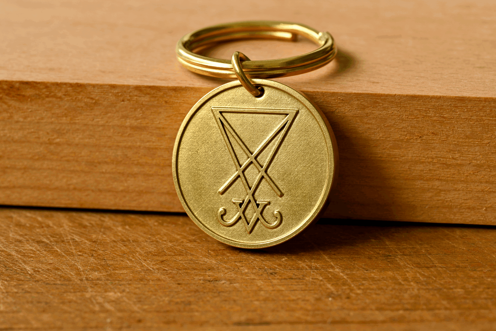 Round brass keychain pendant engraved with the Sigil of Lucifer on a wooden surface