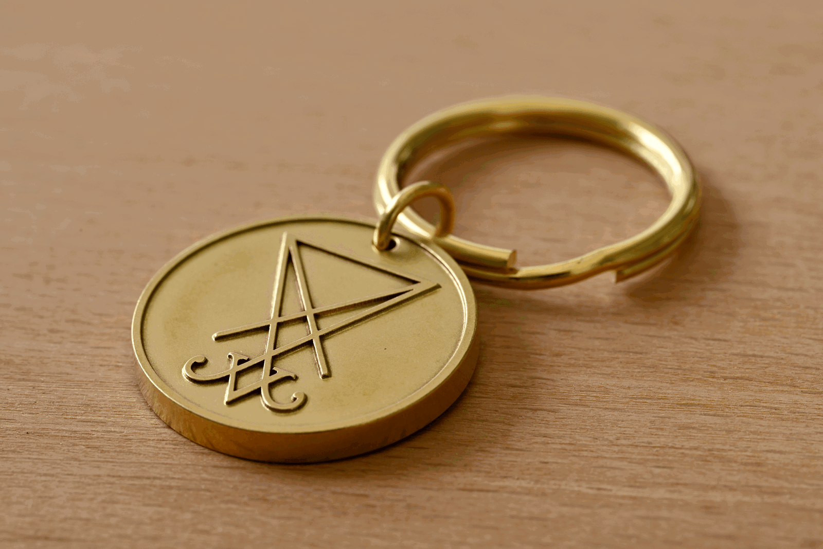 Brass keychain medallion engraved with the Sigil of Lucifer resting on a wooden surface