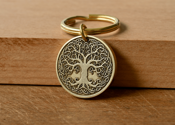 Brass keychain with a circular pendant featuring an intricate Tree of Life design on a wooden background