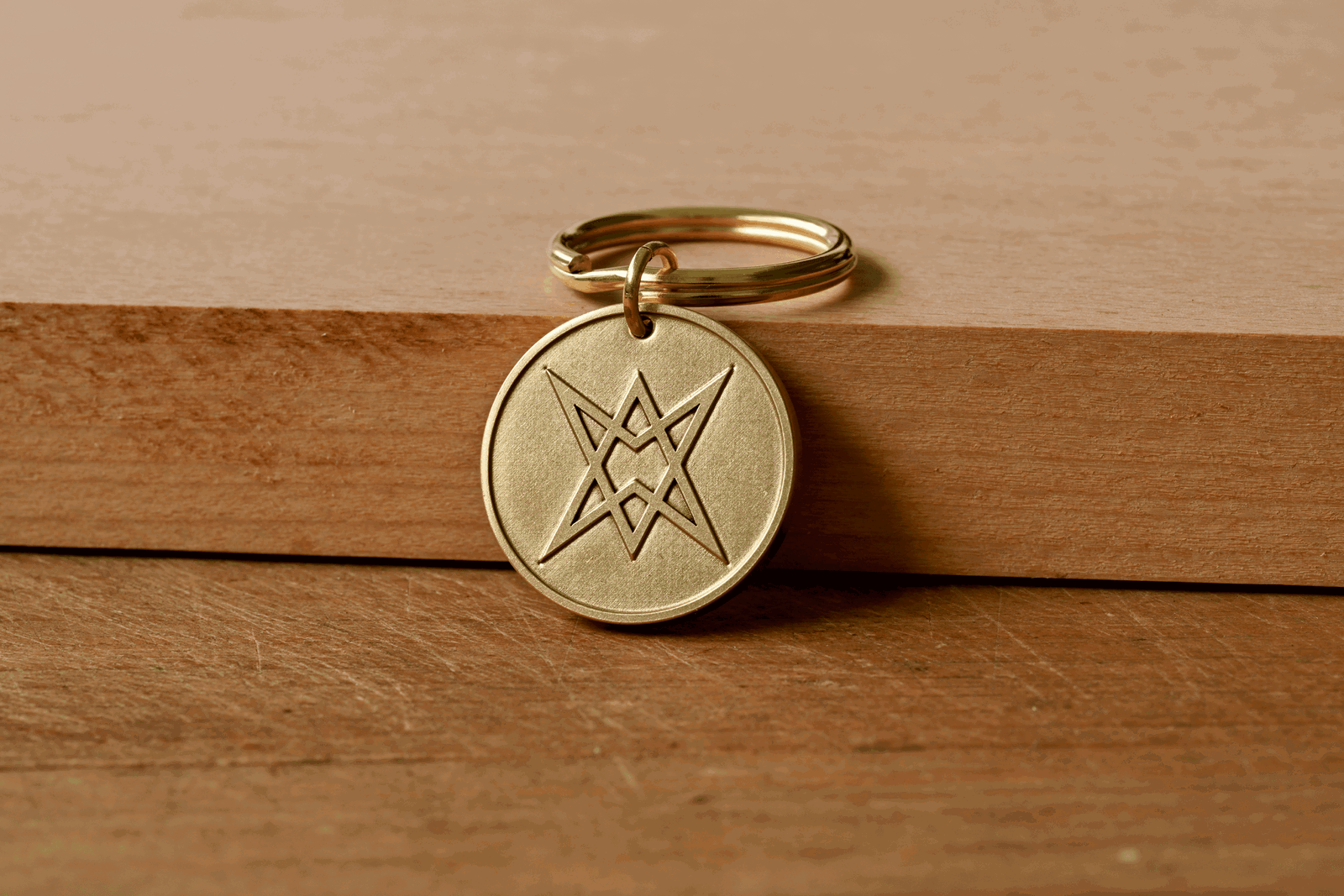 Brass keychain tag with an engraved unicursal hexagram symbol resting on a wooden surface