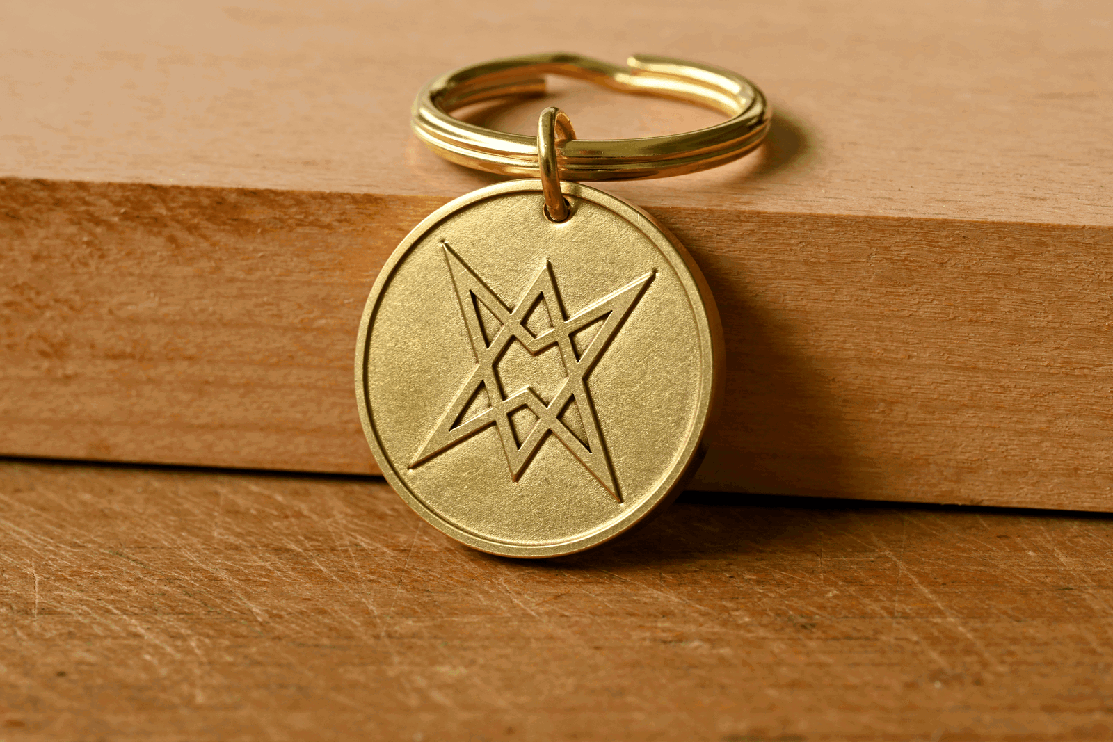 Round brass keychain engraved with a unicursal hexagram symbol resting on a wooden surface