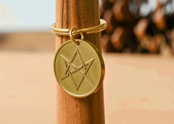 Gold circular keychain tag engraved with a unicursal hexagram hanging on a wooden post