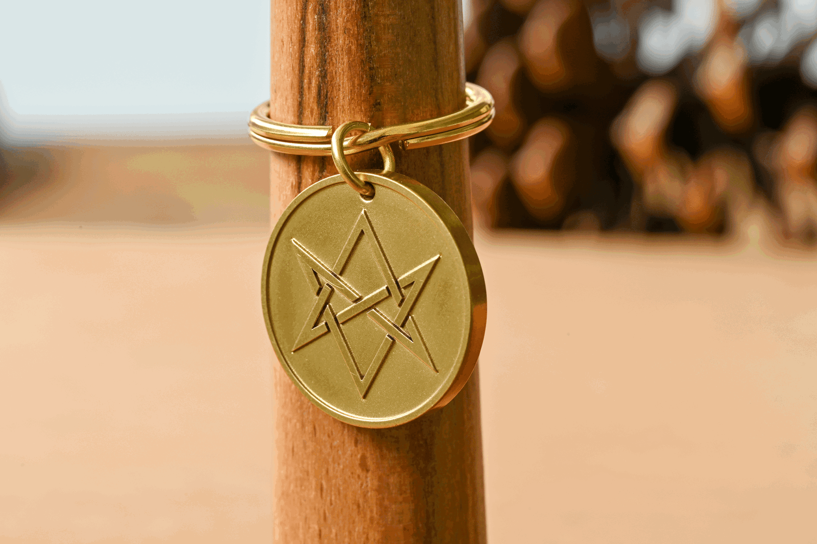 Gold circular keychain tag engraved with a unicursal hexagram hanging on a wooden post