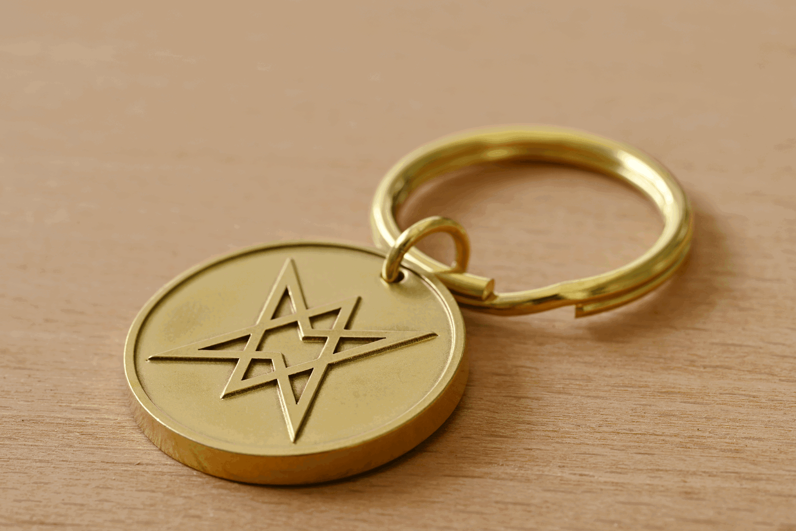 Gold keychain with a circular brass pendant featuring an engraved interlocking star symbol on a wooden surface
