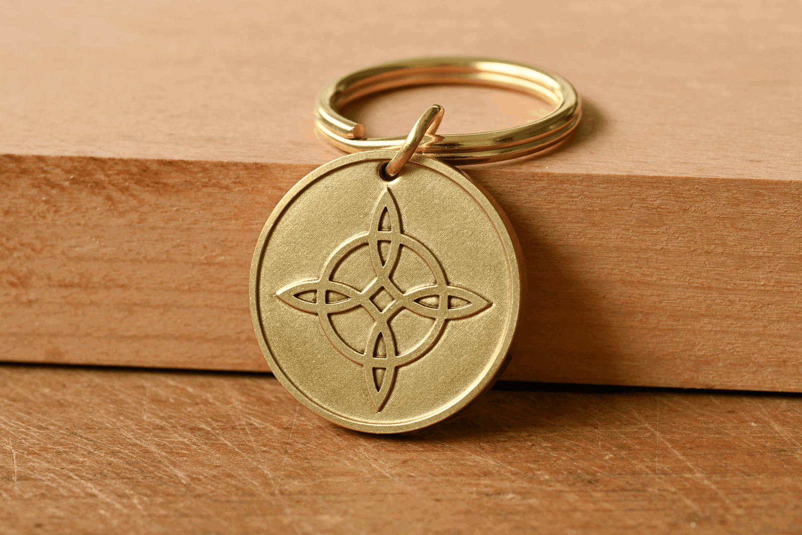 Round brass keychain engraved with a Celtic knot symbol, resting against a wooden block